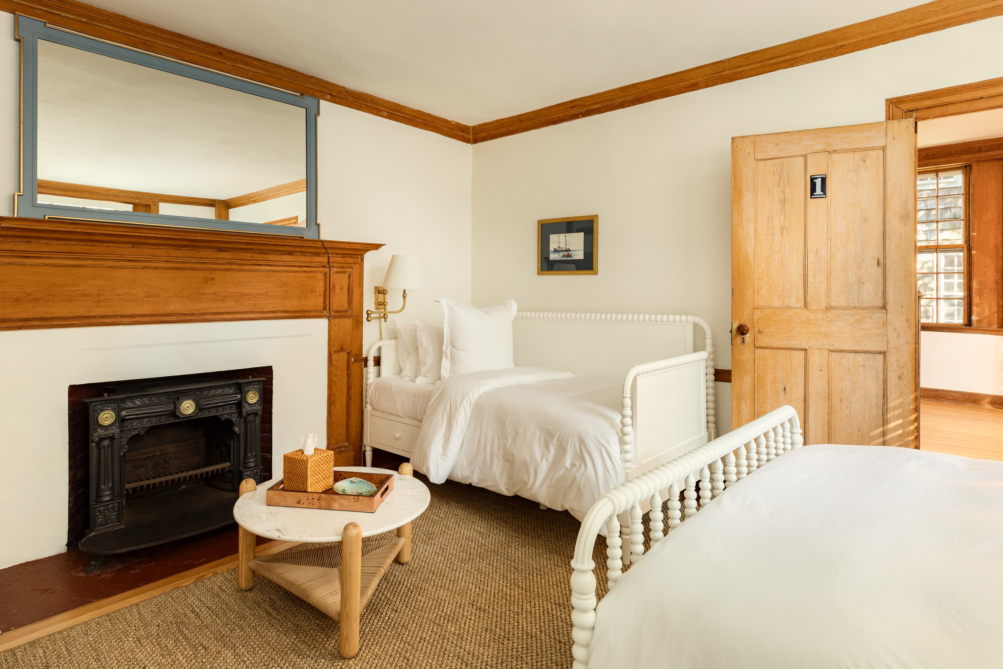 A cozy bedroom featuring a white daybed and a partial view of another bed, a fireplace with a light blue mirror, and wooden accents.
